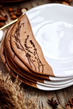 a stack of white plates sitting on top of a wooden table covered in dried plants