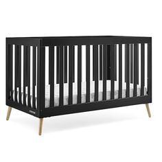 a black crib with white sheets and wood legs on the bottom half, in front of a white background