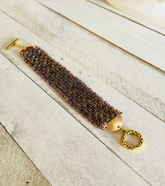 "This hand-woven bracelet was made using 1mm metallic cube gold iris beads, seed beads, faceted glass beads, gold plated endings and gold ornate toggle clasps.  It is 7-1/4\" long and 1\" wide.  It can be lengthened by adding additional jump rings." Bohemian Gold Beaded Crystal Bracelet, Handmade Gold Crystal Bracelet With Round Beads, Handmade Gold Chain Bracelet With Round Beads, Bohemian Gold Crystal Bracelet With Faceted Beads, Gold Beaded Bohemian Chain Bracelet, Gold Crystal Bracelet With Tiny Round Beads, Bohemian Beaded Gold Chain Bracelet, Gold Bohemian Beaded Chain Bracelet, Bohemian Gold Beaded Chain Bracelet