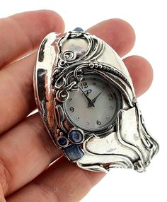 From Porans Watches collection: Sterling silver sturdy elegant gemstone carved cuff bracelet watch gift for love.Unique watch with a  1 pearl (coin)and 4 Kyanite stone inlaid.Dimensions:MaxFront Width: 37 mm.Back width: 12 mm. Size: Can fit any handOur watch is top quality stainless still, analog, Japanese movement with water resistance (up to 3 atmospheres) and it is powered by a battery that lasts about 3 years. The battery can be exchanged.Please notice that because the watch is made to order White Gold Quartz Watches As Gift, Luxury Metal Watches As Gift, Timeless Quartz Jewelry And Watches For Gift, Metal Watch With Metal Dial As A Gift, Gift Polished Round Dial Jewelry And Watches, Timeless Metal Jewelry And Watches For Gifts, Timeless Metal Jewelry And Watches As Gifts, Luxury Metal Watch As Gift, Elegant Metal Jewelry And Watches For Gifts