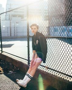 a woman in black shirt and shorts sitting on the side of a fence with her legs crossed