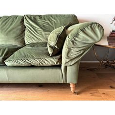 a green couch sitting on top of a hard wood floor next to a wooden table