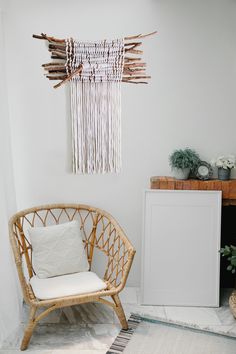 a wicker chair sitting in front of a wall hanging on the side of a white wall