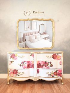 a white dresser with pink flowers painted on it and a gold frame around the mirror