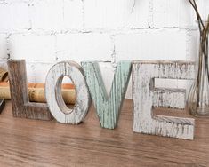 the word love is made out of wood and sits on a shelf next to a vase with flowers