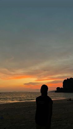 a man standing on top of a sandy beach next to the ocean at sunset or dawn