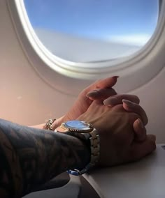 two people holding hands while sitting on an airplane with the window looking out at the sky