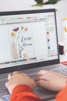 a person using a laptop computer on a desk with flowers and the words love is written on the screen