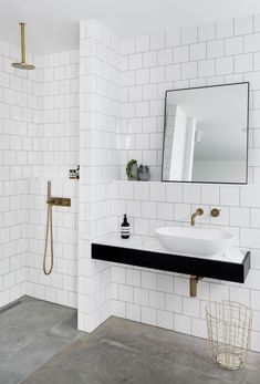 a white tiled bathroom with black counter tops and gold faucet, along with a mirror above the sink