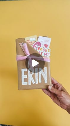 a person holding up a brown paper bag with the word erin on it and pink ribbon