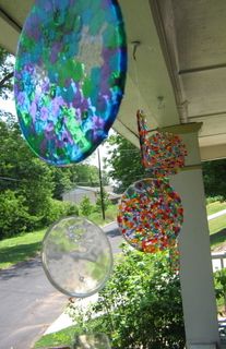 some glass balls hanging from the side of a house with trees and bushes in the background