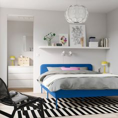 a bed room with a neatly made bed next to a chair and a shelf on the wall