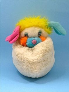 a white stuffed animal with yellow hair and pink nose sitting in a ball on a blue background