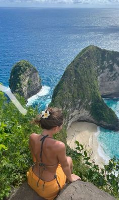 a woman sitting on top of a cliff overlooking the ocean