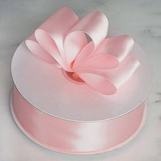 a pink satin ribbon on top of a white box with a large bow at the top