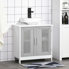 a bathroom with a white sink and gray cabinet next to a black and white rug