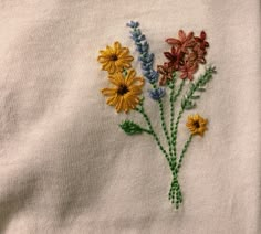 embroidered flowers on a white shirt with green stems and yellow daisies in the center