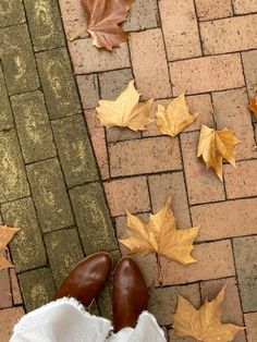 a person's feet in white pants and brown shoes with leaves on the ground