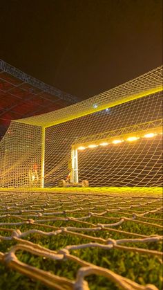 a soccer goal with the lights on and grass in front of it at night time