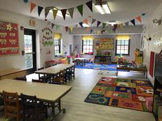 a classroom with tables, chairs and rugs on the floor in front of windows