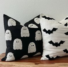 two black and white halloween pillows with bats on them sitting on a wooden table in front of a gray wall