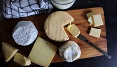 several different types of cheese on a wooden cutting board next to a glass of milk