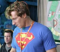 a man in a superman t - shirt is looking at his cell phone while standing next to another man