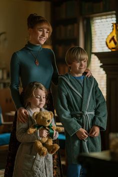 three children standing next to each other with a teddy bear in front of them,