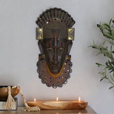 an african mask hanging on the wall next to a candle holder and potted plant