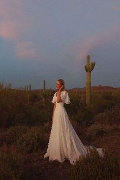 a woman in a white wedding dress standing next to a large saguado cactus