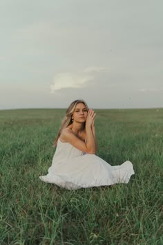 a woman sitting in the middle of a field with her hands up to her face