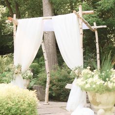 an outdoor wedding ceremony with white drapes and flowers in vases on the ground