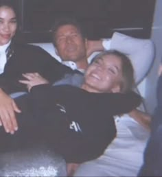 two women and a man laying on a bed with their arms around each other smiling