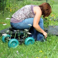 a woman kneeling down in the grass next to a lawn mower with wheels on it