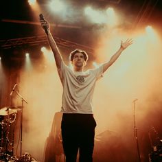 a young man standing on stage with his arms in the air and lights behind him