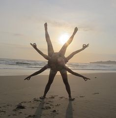 two people are standing on the beach with their arms in the air as the sun sets