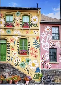 a building with flowers painted on it's side next to a bike and flower potted planter