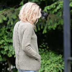 a woman standing in front of some trees wearing a cardigan sweater and ripped jeans