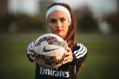 a young woman holding a soccer ball in her right hand and wearing a headband