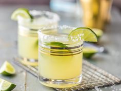 two glasses filled with lemonade and limes on top of a metal tray next to some sliced limes