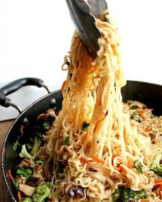 someone is lifting noodles from a skillet filled with broccoli and other vegetables