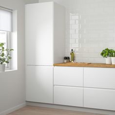 a kitchen with white cabinets and wooden counter tops next to a potted plant on a window sill