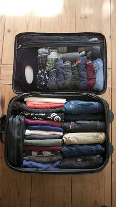 an open suitcase filled with clothes on top of a wooden floor