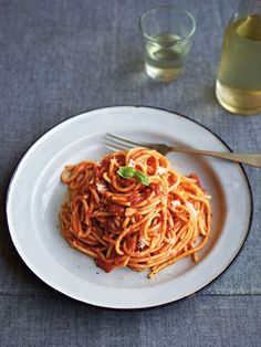 a white plate topped with spaghetti and sauce next to a glass of olive oil on a table