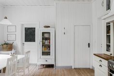 a kitchen with white walls and wood flooring next to a dining room table in the center