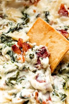 a tortilla chip being dipped with cheese and spinach dip in a bowl