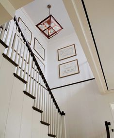 a staircase with pictures on the wall next to it and a light fixture hanging from the ceiling