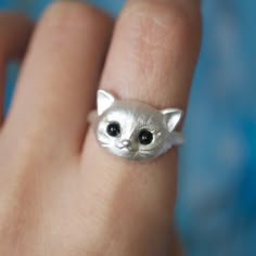 a close up of a person's hand with a cat ring on their finger