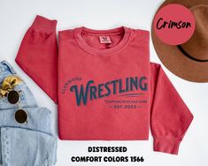 a pair of jeans and a red shirt with the words wrestling on it next to a hat