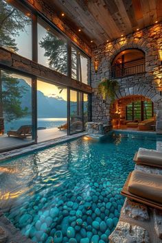 an indoor swimming pool surrounded by stone walls and flooring, with large windows overlooking the water